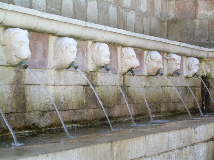 a bunch of stone water fountains with head sculptures on them