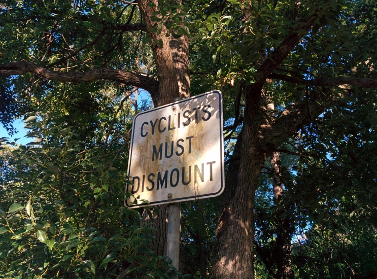 a sign on a pole reads cyclists must discurs on dirt