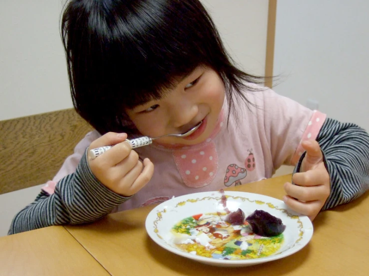 a girl sitting at a table eating cake with a fork