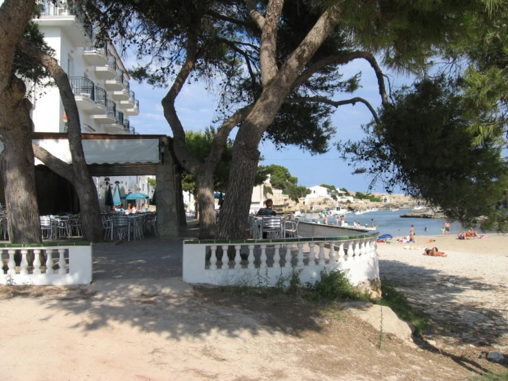 an open air deck and table area under some trees by the beach