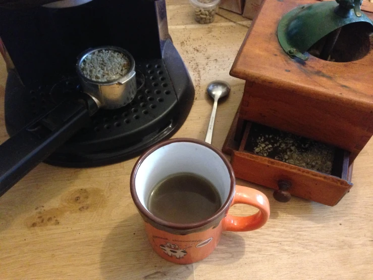 a cup of coffee on the table beside the grinder and grinder