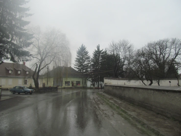 a rainy street with parked cars and houses in the background