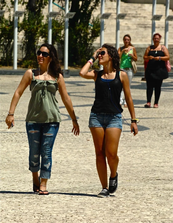 two young ladies wearing sunglasses are walking on the beach