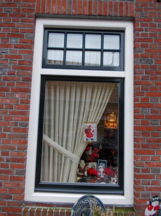 a brick wall has an open window with white curtains