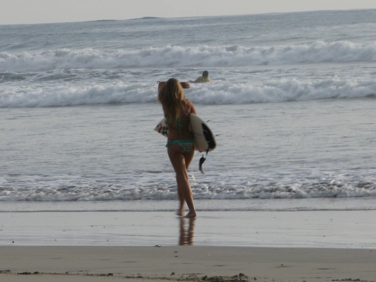woman in bikini carrying a surfboard while walking along a beach