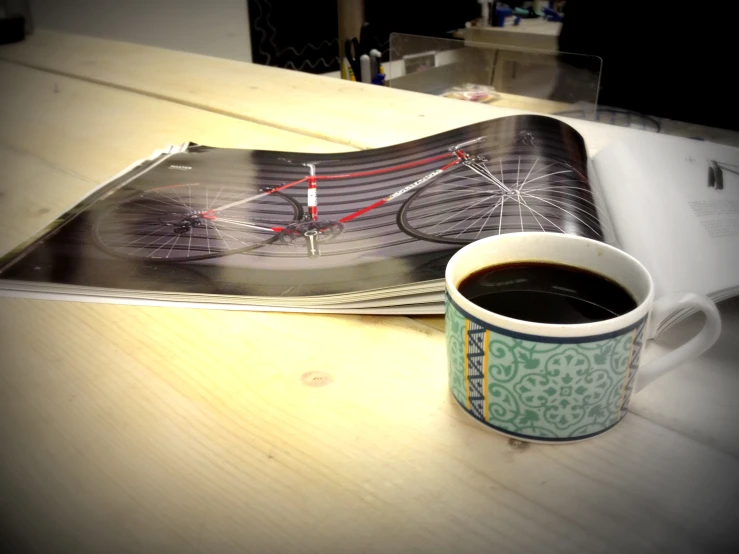 a cup of coffee and book are set on a wooden desk