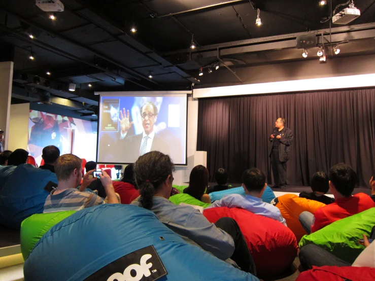 a man speaking to a group of people in front of a screen