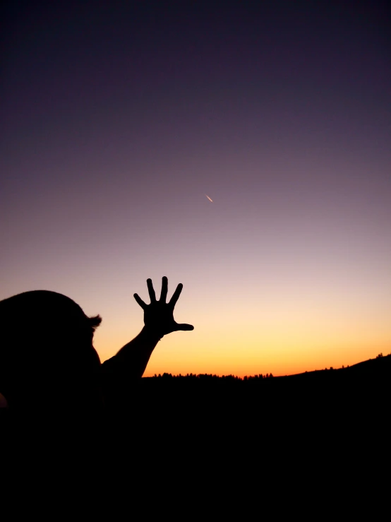 the silhouette of a person's arm and hand with the sky in the background