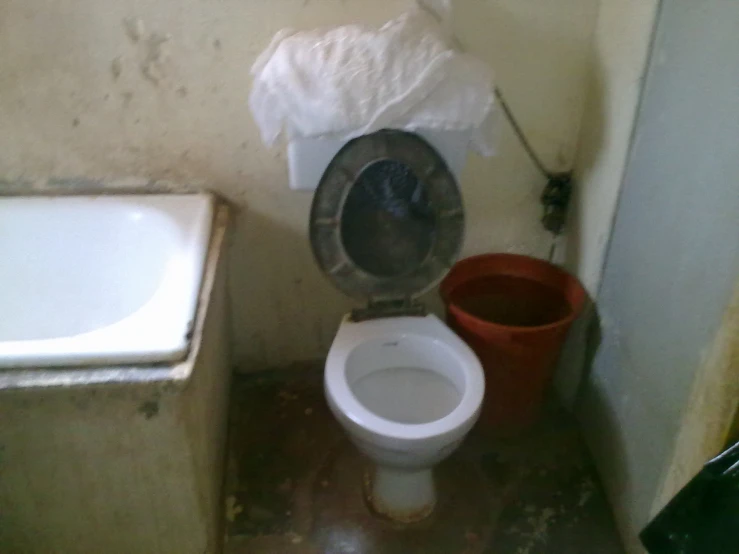 a small dirty bathroom with an old toilet and trash can