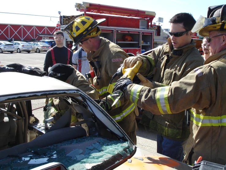 firemen help with the windshield to make a damaged car