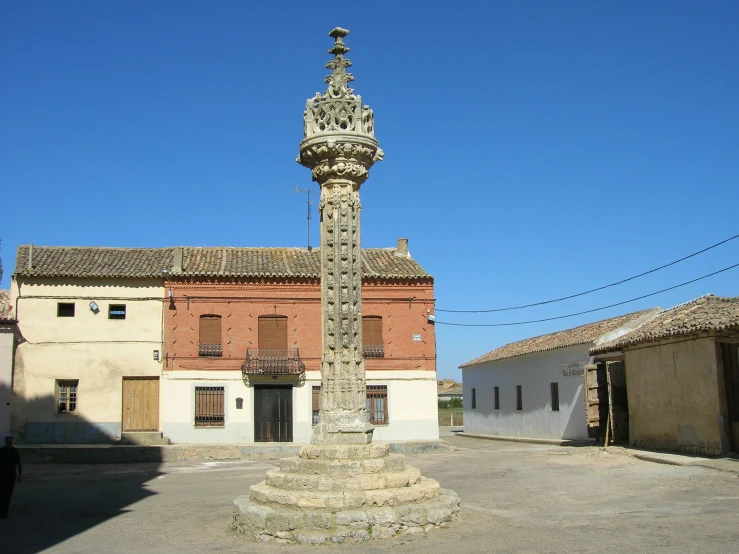 a stone pole with a clock on top in the middle of some buildings
