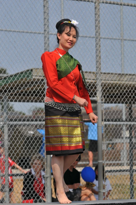 a woman wearing an orange shirt standing in front of a fence