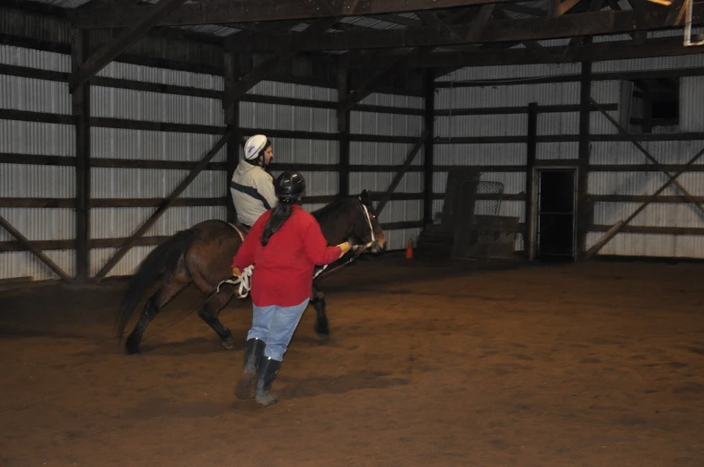 woman walking a horse in a barn while she rides