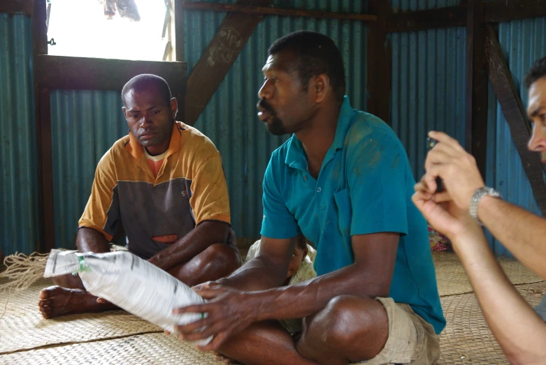 three men sitting on the floor of a hut