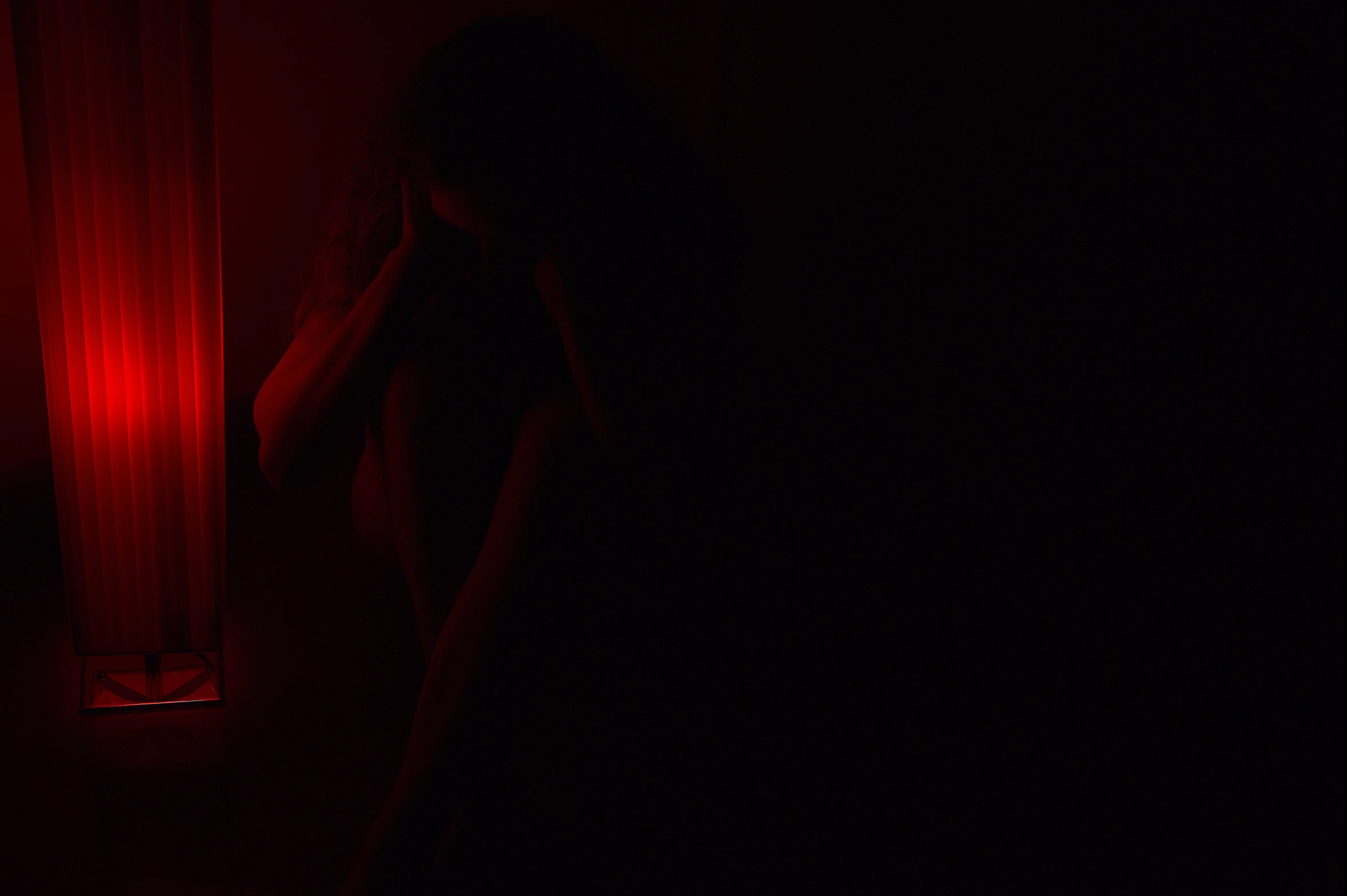 a person standing in a dark room, holding their head in their hands