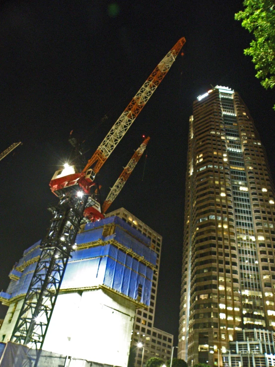 the two building are tall and have many cranes around it