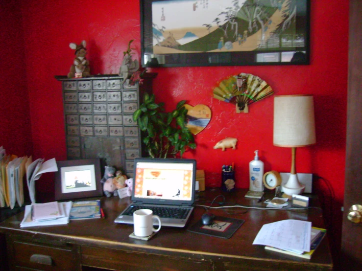 a cluttered desk with a laptop computer, books, papers and a fan