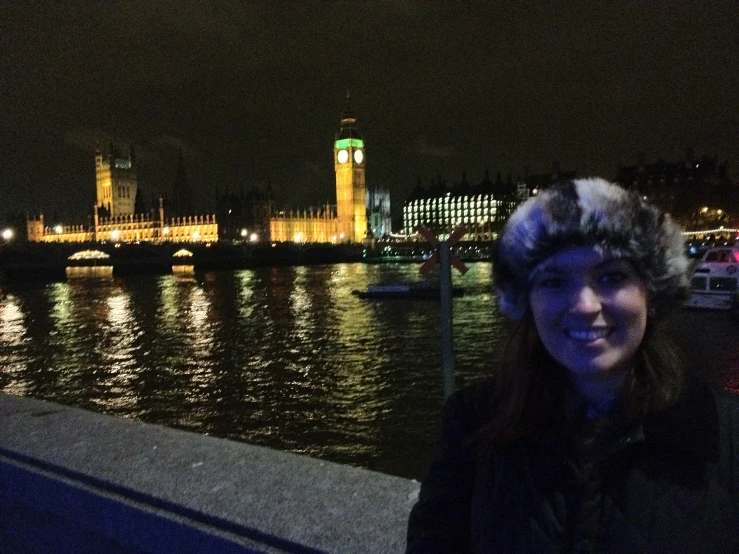 a woman poses with big ben at night by the river thames in london