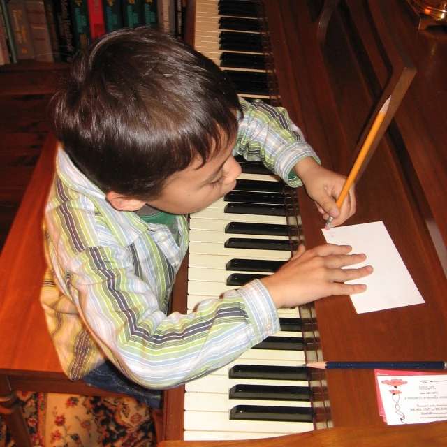 a boy in striped shirt writing in front of an organ