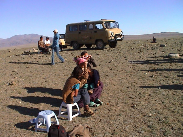 people sit and stand near the vehicle in a desert