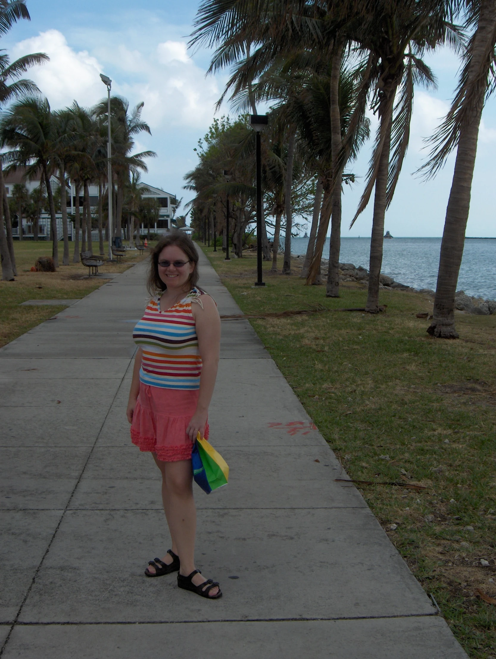 woman standing at sidewalk with palm trees beside water