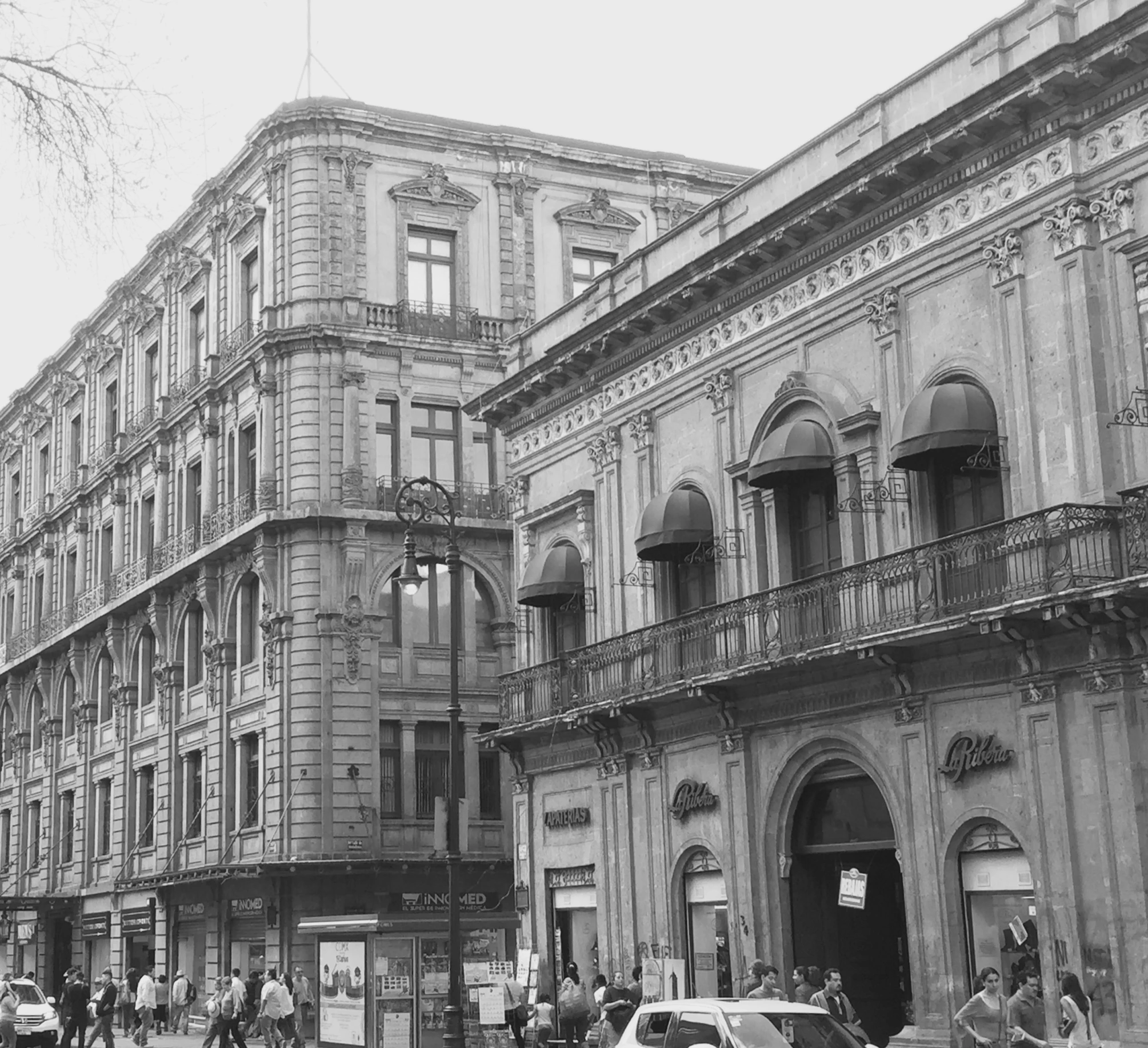 black and white po of people walking on sidewalk near buildings