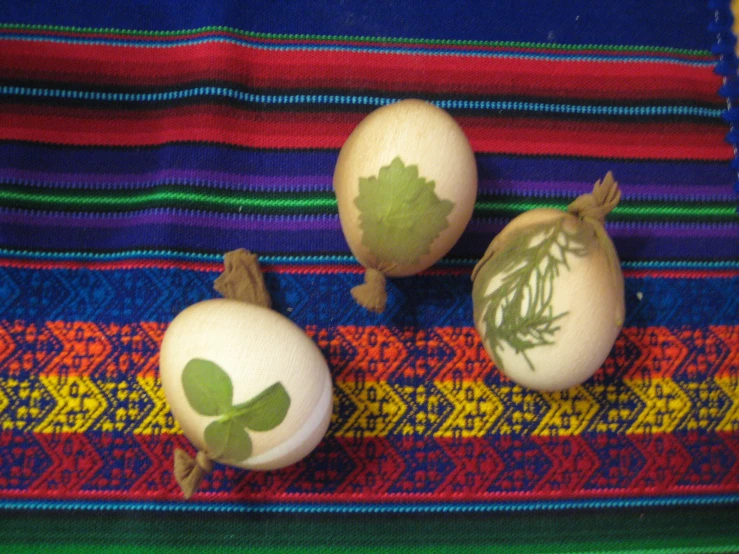 three eggs on colored striped fabric and each one has painted leaves