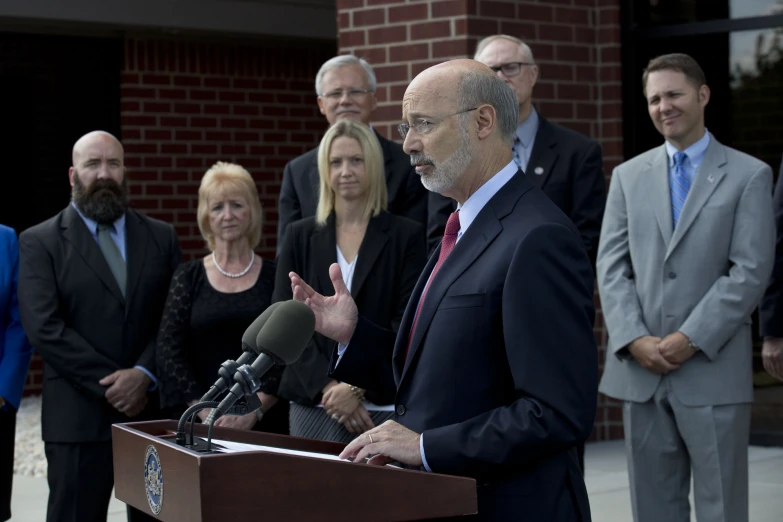 a man in suit speaking from a podium next to a group of people