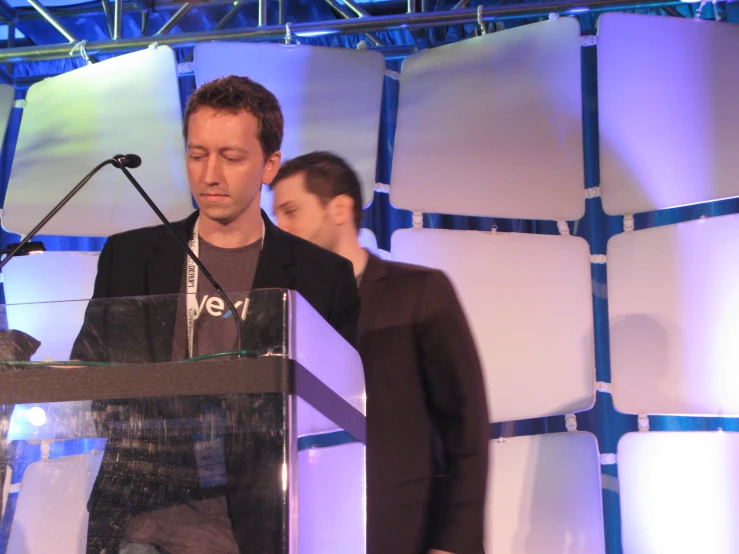 two people are on stage and one man is standing in front of a large podium