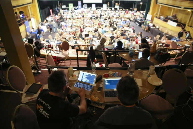 two men sit on a large table with laptops in front of them