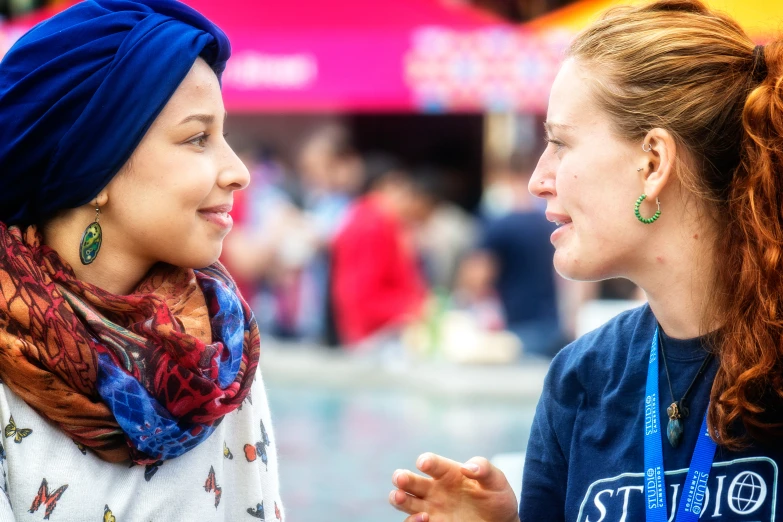 two young women are talking and smiling in front of a crowd