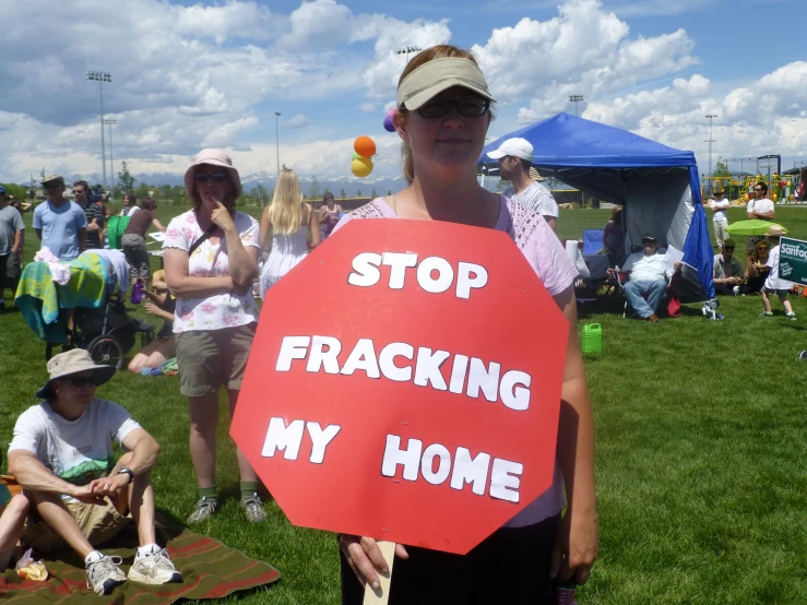 a woman holds a stop franacking sign in a grassy area