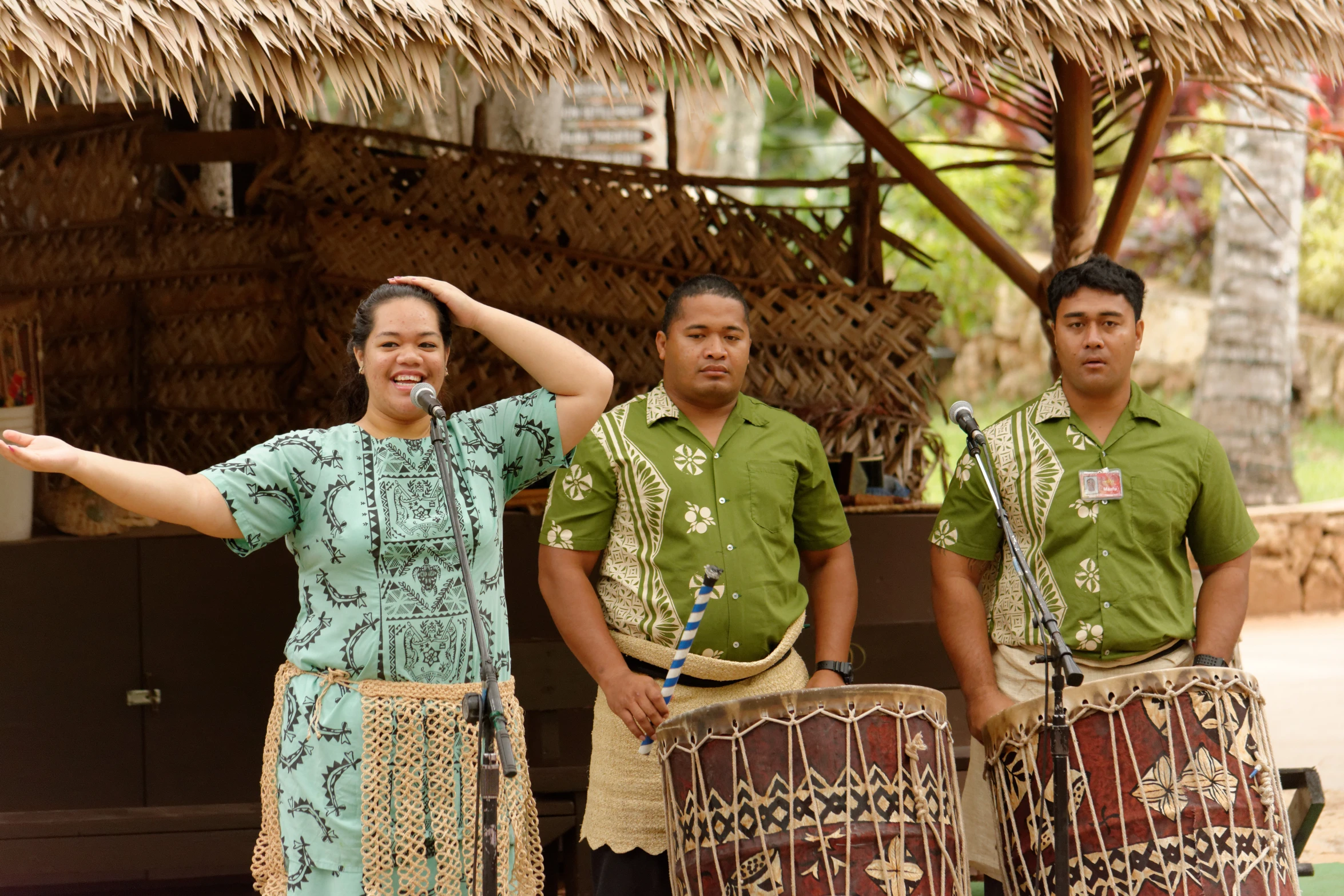 a woman and two men with drums stand next to an african hut