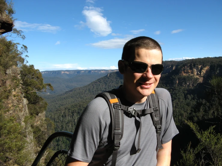 a man wearing sunglasses standing on the top of a mountain