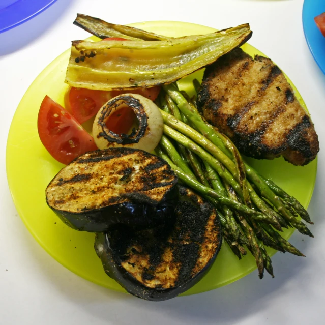 a plate of grilled pork, green beans, tomato, asparagus and a potato wedges