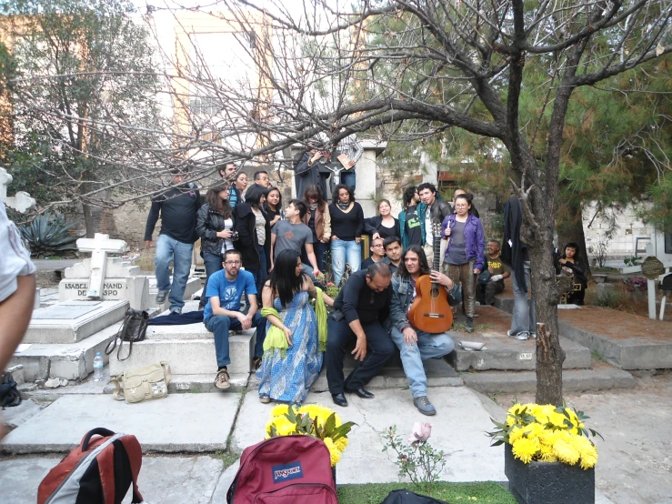 a group of people are sitting around near a tree and flower arrangement