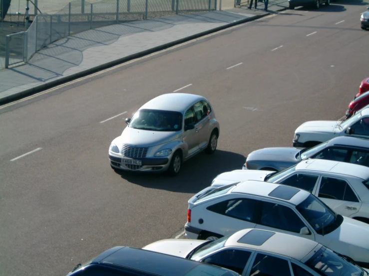 a silver car driving down a street next to a fence