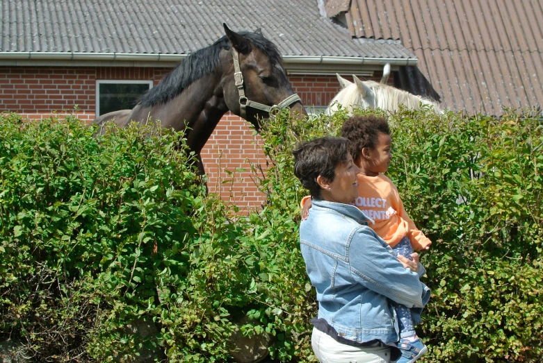 the woman is holding her son in front of the horse