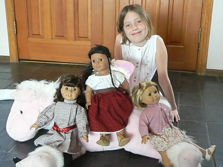 a little girl is sitting with her three doll set