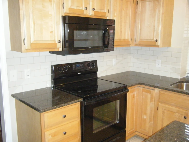 an all black kitchen with a wood grain cabinetry and granite countertops