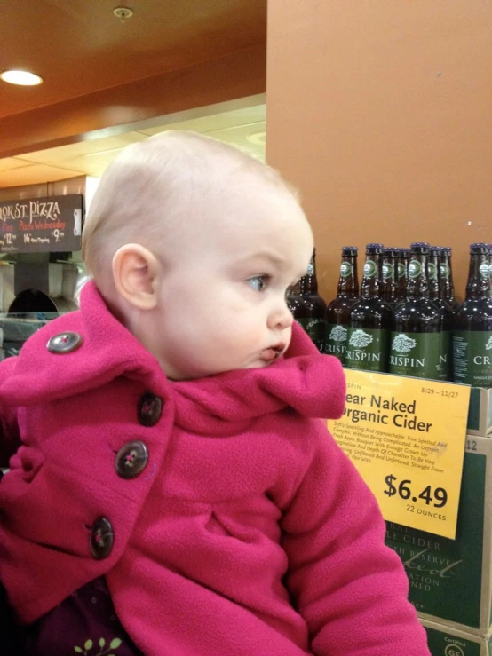 a baby girl in a pink coat is looking at the bottle