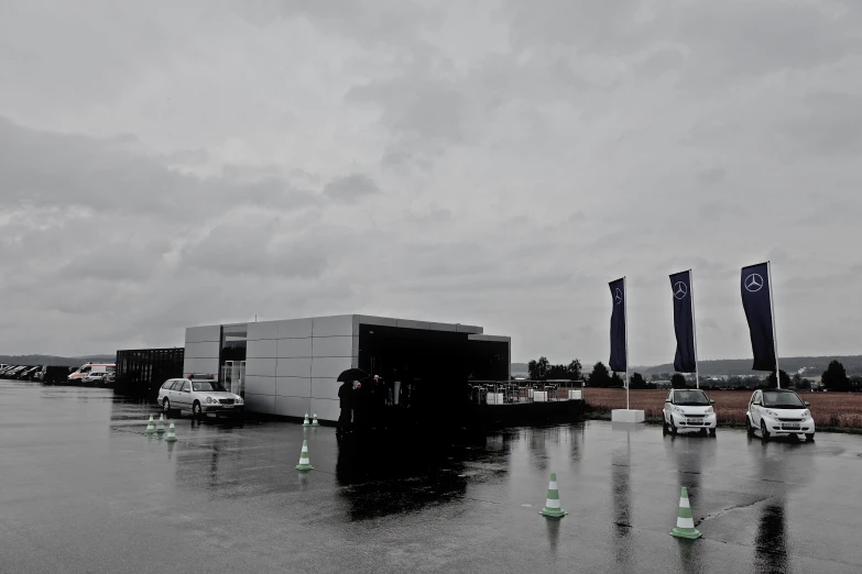 two flags on a dark and cloudy day with cars parked outside of them