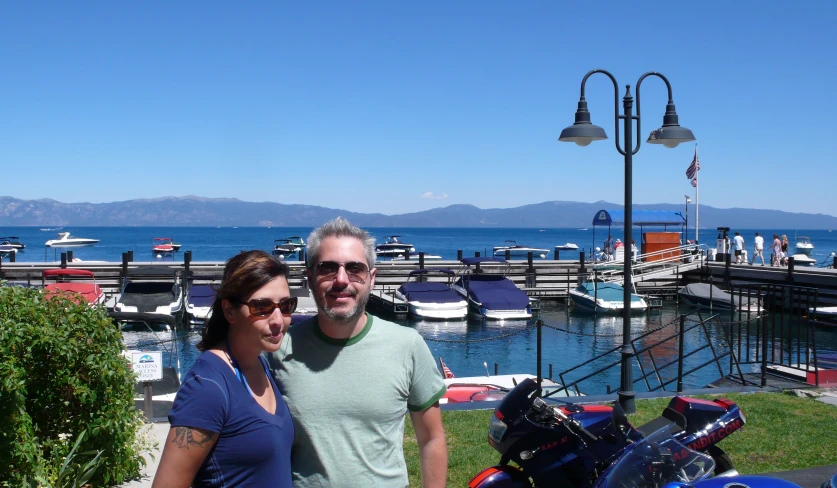 a couple standing in front of a motor bike with a view of water