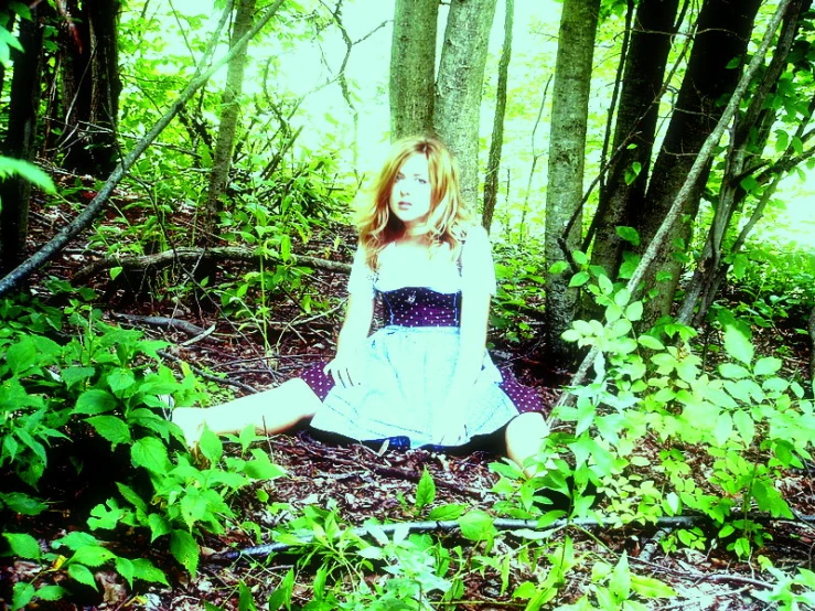 a girl sits on the ground in the woods