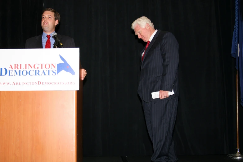 two men in suits stand at a podium and look to the side