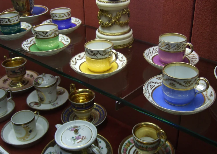 many different colored cups and saucers and on display behind a glass