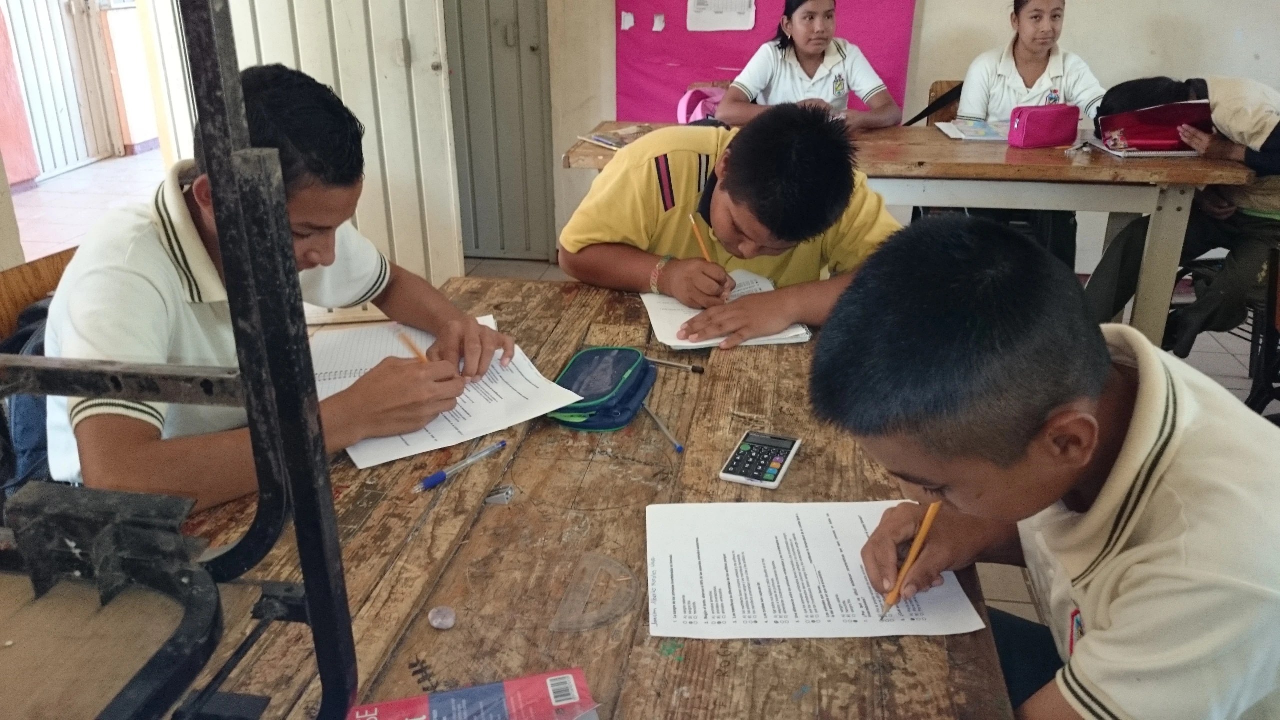 several boys in a room sitting at a table working on some paper