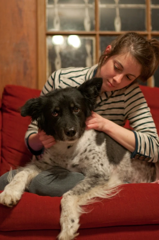 a woman sits on a red couch while petting a dog