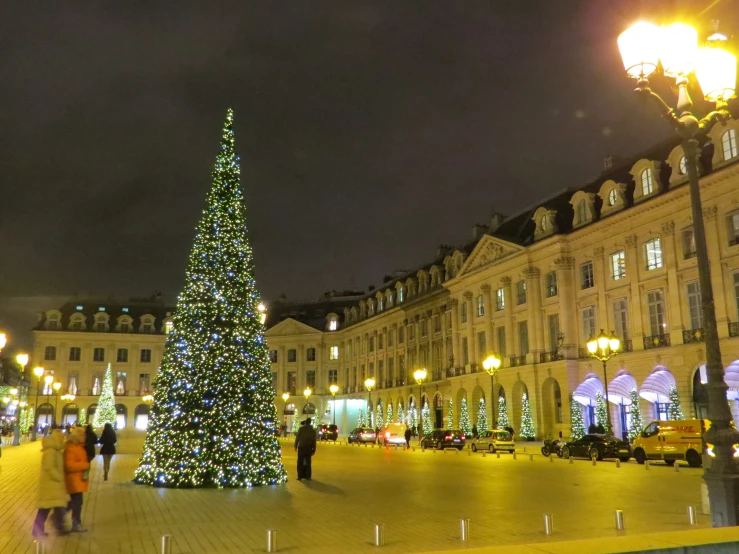 people walking in front of a lit up christmas tree