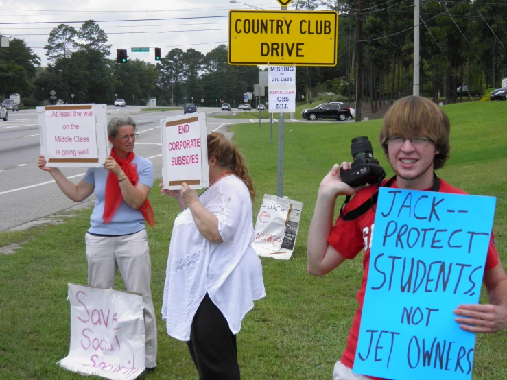 three people are standing in the grass with signs